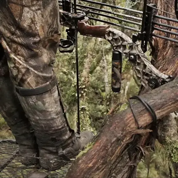 Close up of bow hunter standing in tree, resting bow